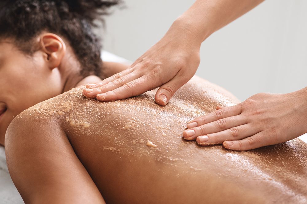 Hands massaging a person’s back with exfoliating scrub in a spa setting