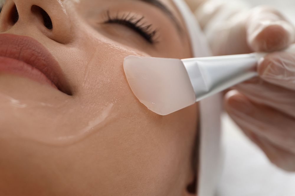 Facial skincare treatment with a cream mask being applied to a woman’s cheek with a brush